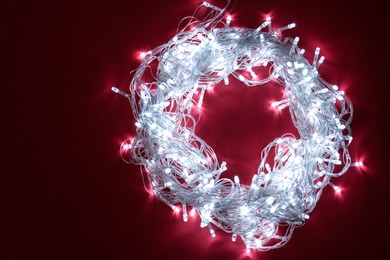 Photo of Frame made of glowing Christmas lights on burgundy background, top view. Space for text