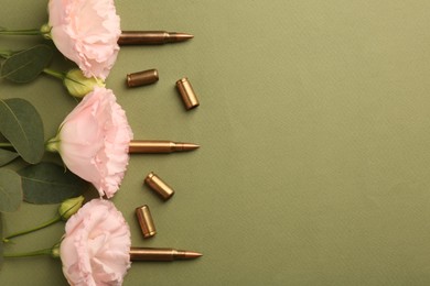 Bullets, cartridge cases and beautiful eustoma flowers on green background, flat lay. Space for text
