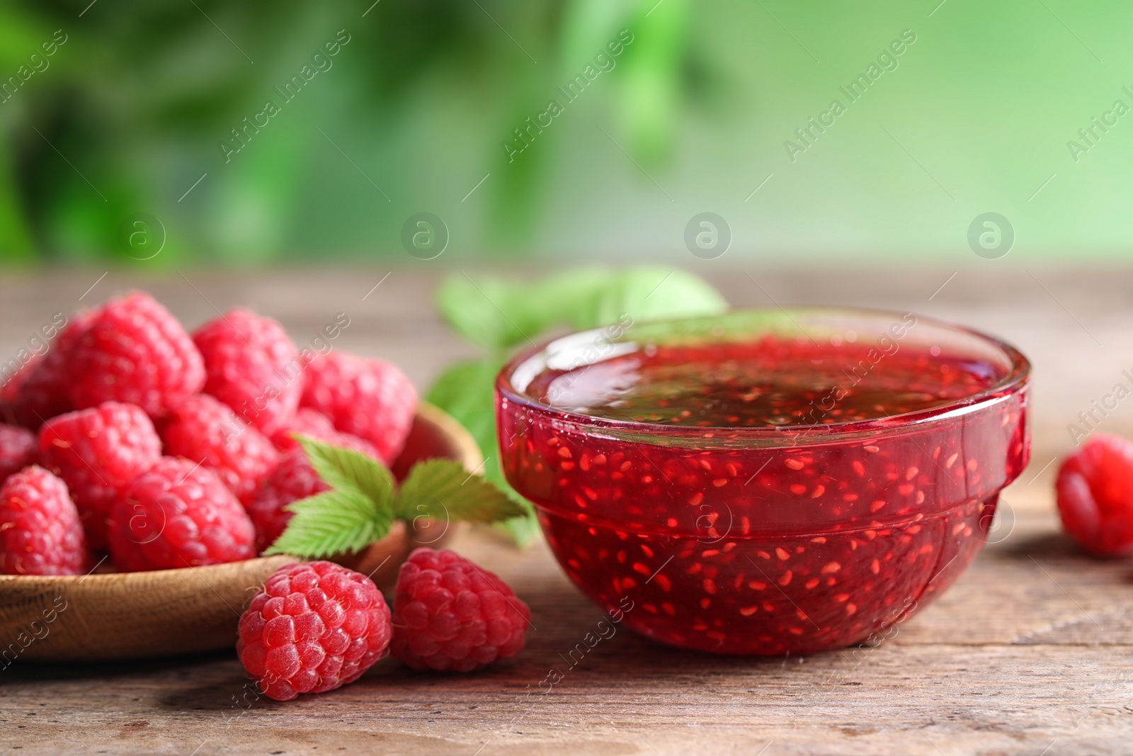 Photo of Bowl of sweet jam with ripe raspberries on wooden table, closeup