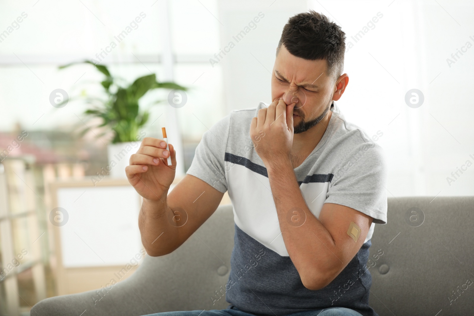 Photo of Emotional man with nicotine patch and cigarette at home