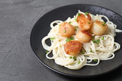 Photo of Delicious scallop pasta with green onion on grey table, closeup. Space for text