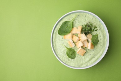 Delicious spinach cream soup with croutons in bowl on green background, top view. Space for text