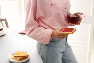 Woman having tasty breakfast with toast and raspberry tea at home, closeup. Morning routine