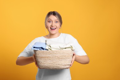 Emotional woman with basket full of laundry on orange background