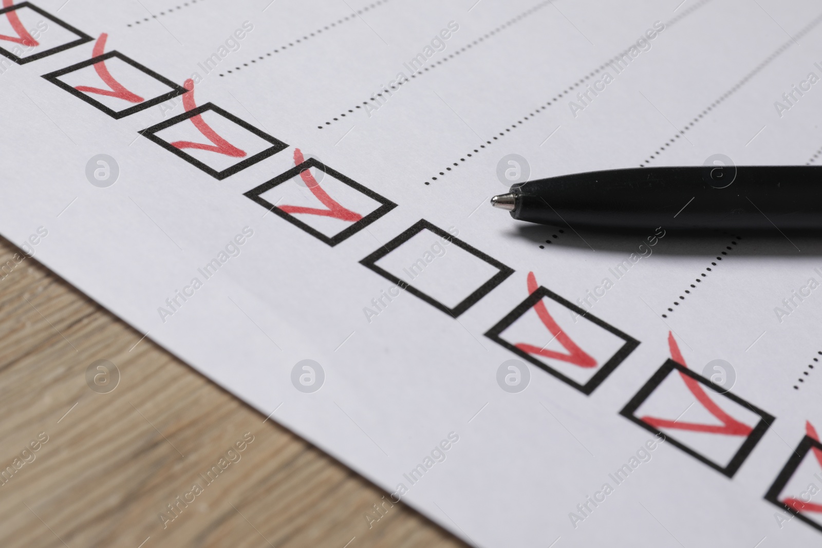 Photo of Paper sheet with checkboxes and pen on wooden table, closeup. Checklist