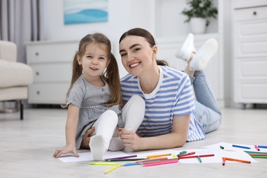 Photo of Mother and her little daughter drawing with colorful markers on floor at home