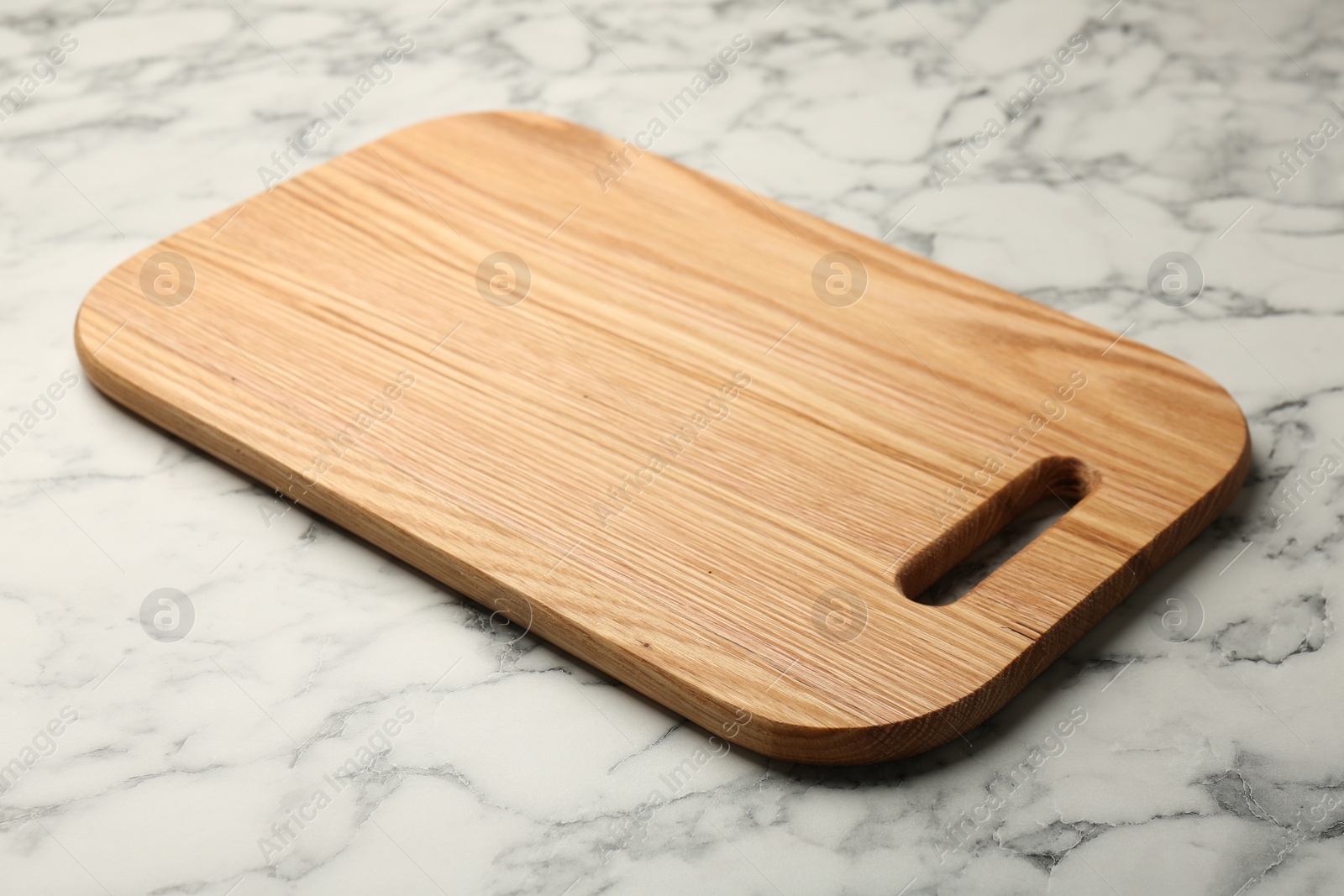 Photo of Wooden cutting board on white marble table, closeup