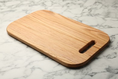 Photo of Wooden cutting board on white marble table, closeup