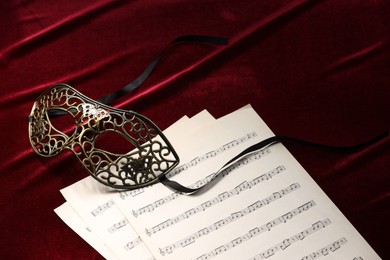 Photo of Elegant face mask and music sheets on red fabric. Theatrical performance