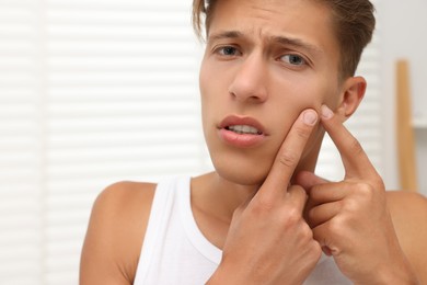 Photo of Upset young man popping pimple on his face indoors. Acne problem