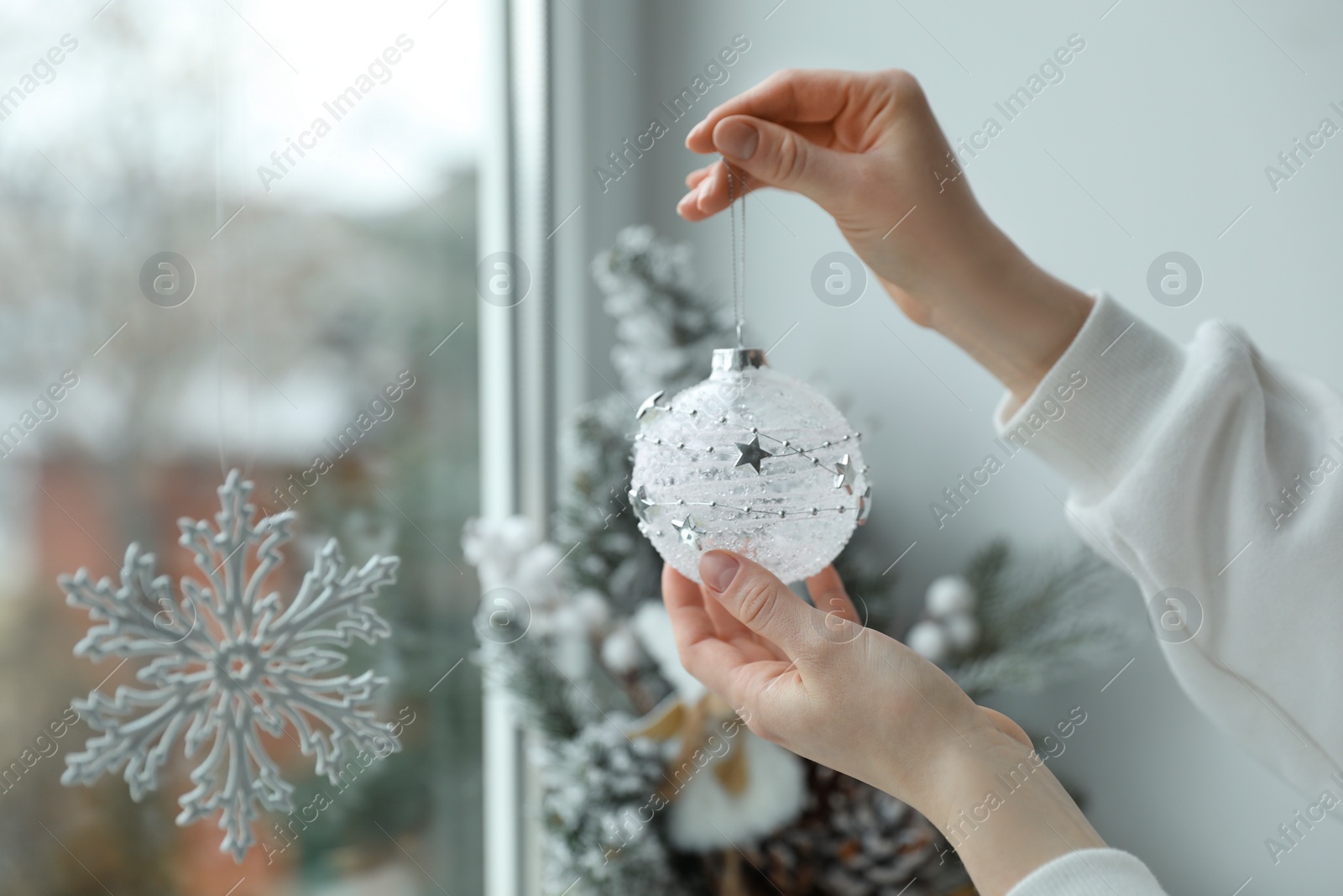 Photo of Woman holding Christmas bauble near window indoors, closeup