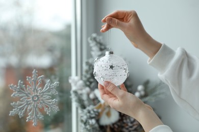 Woman holding Christmas bauble near window indoors, closeup
