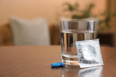 Photo of Glass of water, condom and pills on wooden table indoors, space for text. Potency problem concept
