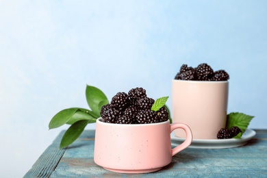 Photo of Mug with fresh blackberry on table against color wall