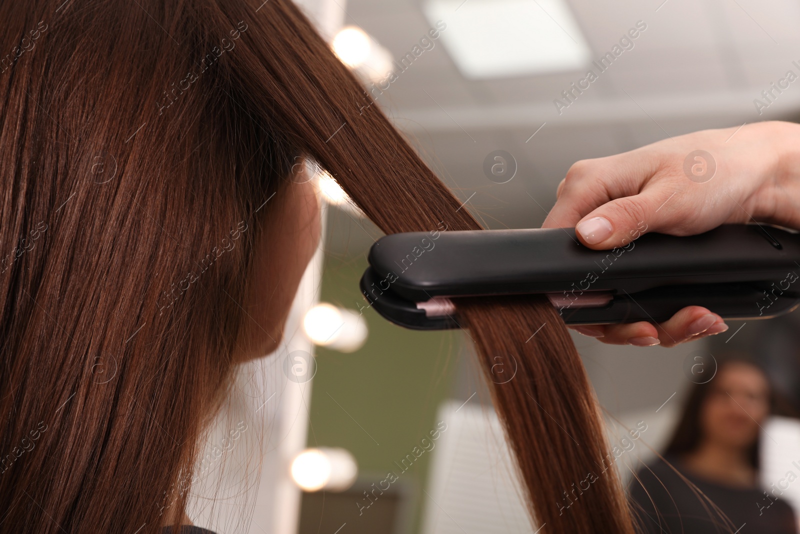 Photo of Stylist straightening woman's hair with flat iron in salon