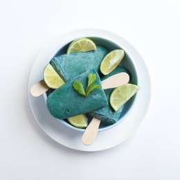 Photo of Bowl with delicious spirulina popsicles and lime slices on white background, top view