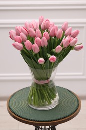 Bouquet of beautiful pink tulips in vase on table near white wall