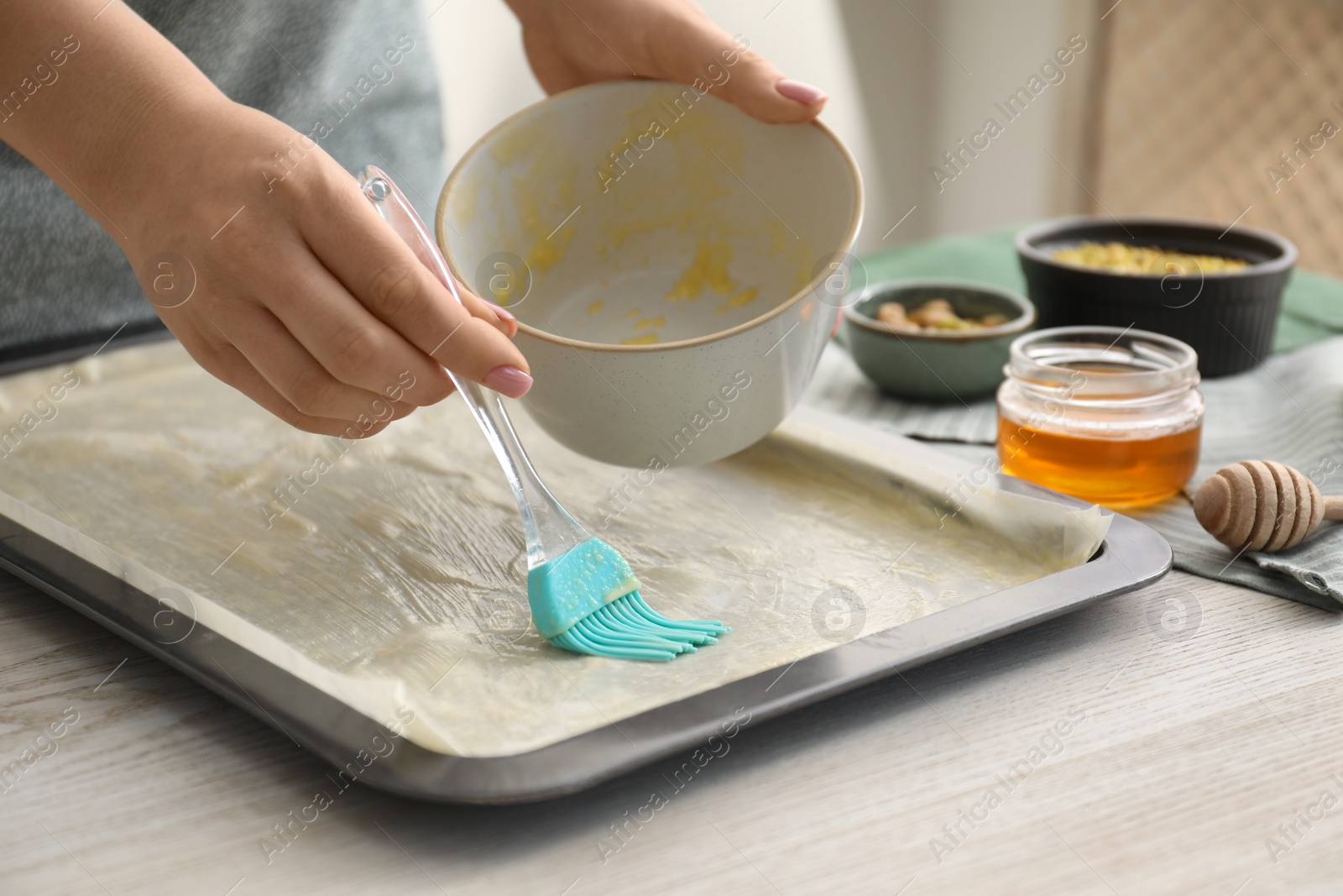 Photo of Making delicious baklava. Woman buttering dough in baking pan at white wooden table, closeup