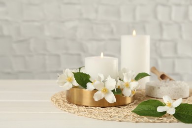 Photo of Beautiful jasmine flowers and burning candles on white wooden table, space for text