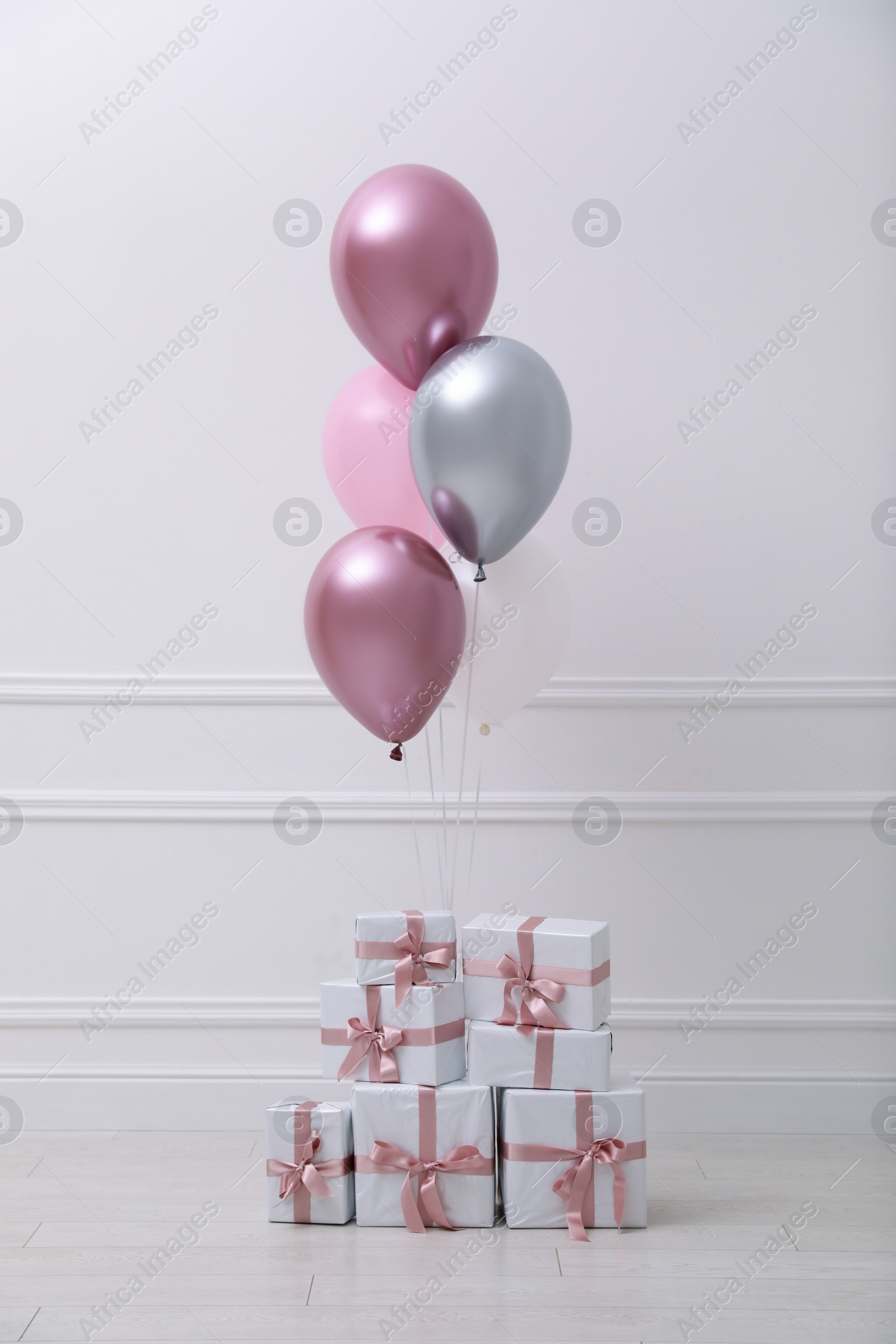 Photo of Many gift boxes and balloons near white wall in room