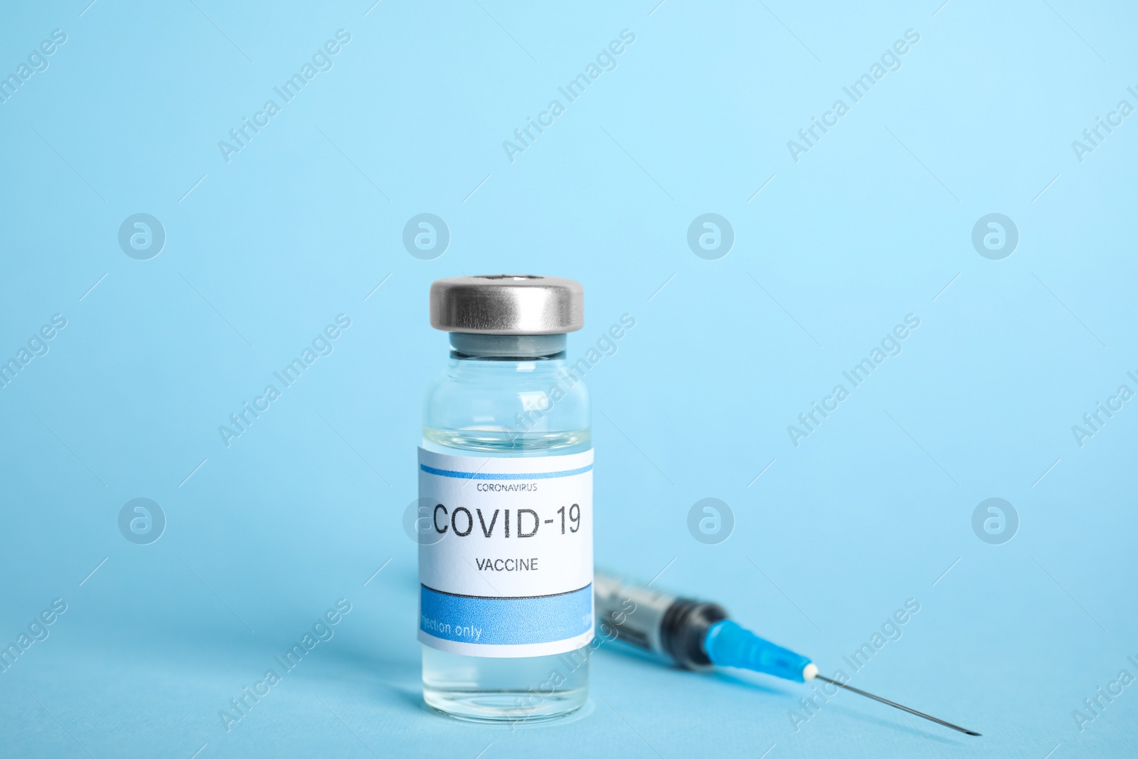 Photo of Vial with coronavirus vaccine and syringe on light blue background