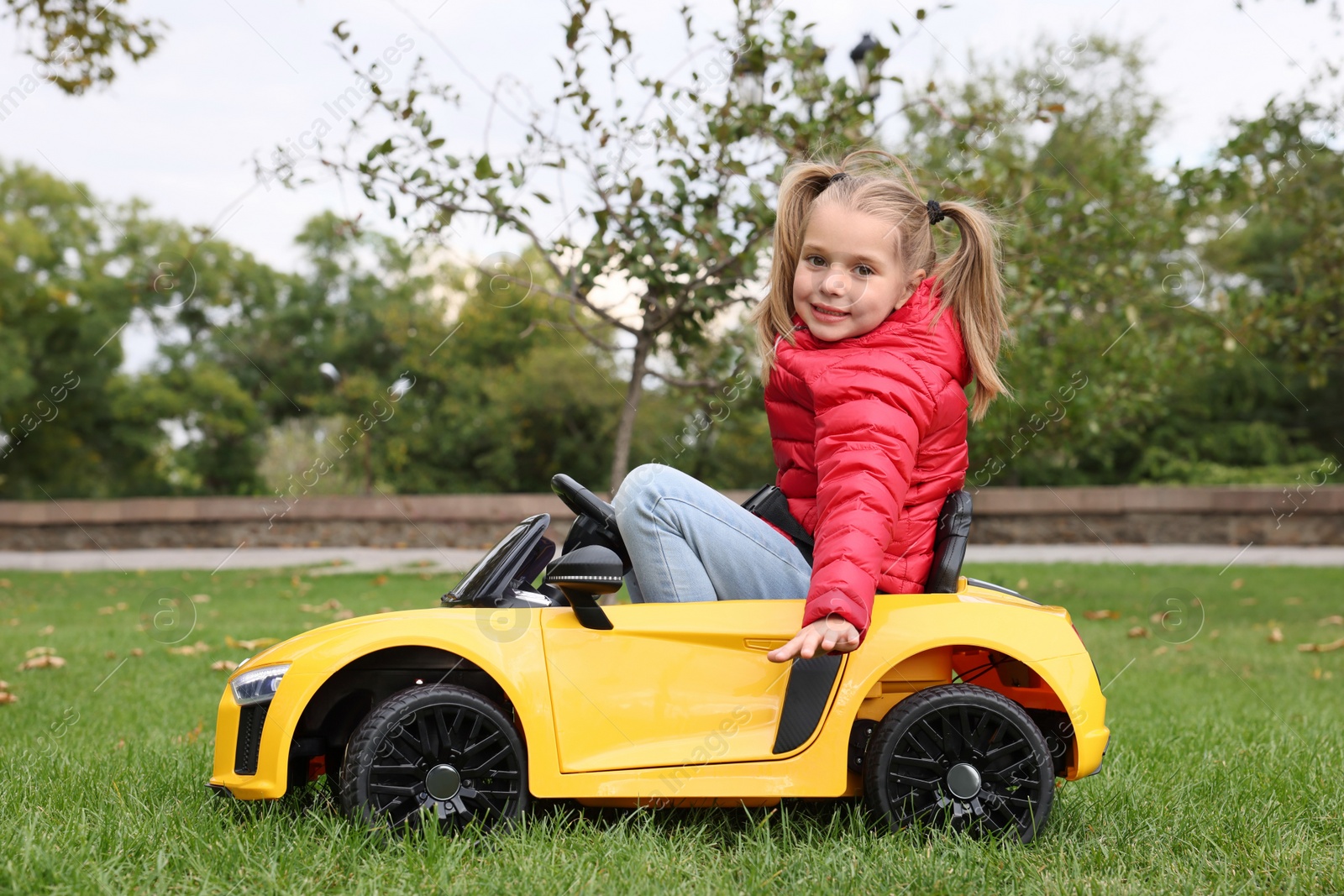 Photo of Cute little girl driving children's car in park