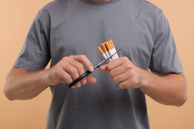 Stop smoking concept. Man cutting cigarettes on light brown background, closeup