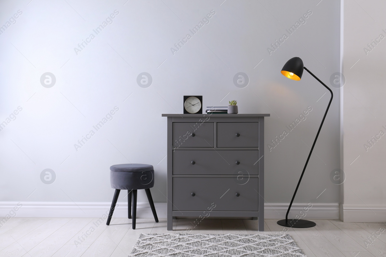 Photo of Elegant room interior with stylish chest of drawers, pouf and floor lamp