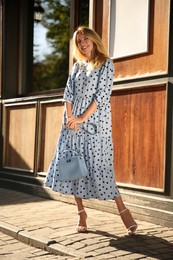 Photo of Beautiful young woman in stylish light blue polka dot dress with handbag on city street