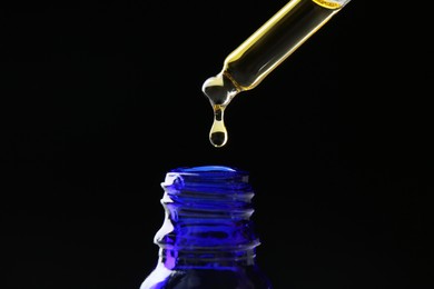 Photo of Dripping tincture from pipette into bottle on black background, closeup