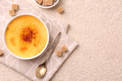 Photo of Delicious creme brulee in bowl, sugar cubes and spoon on light textured table, top view. Space for text