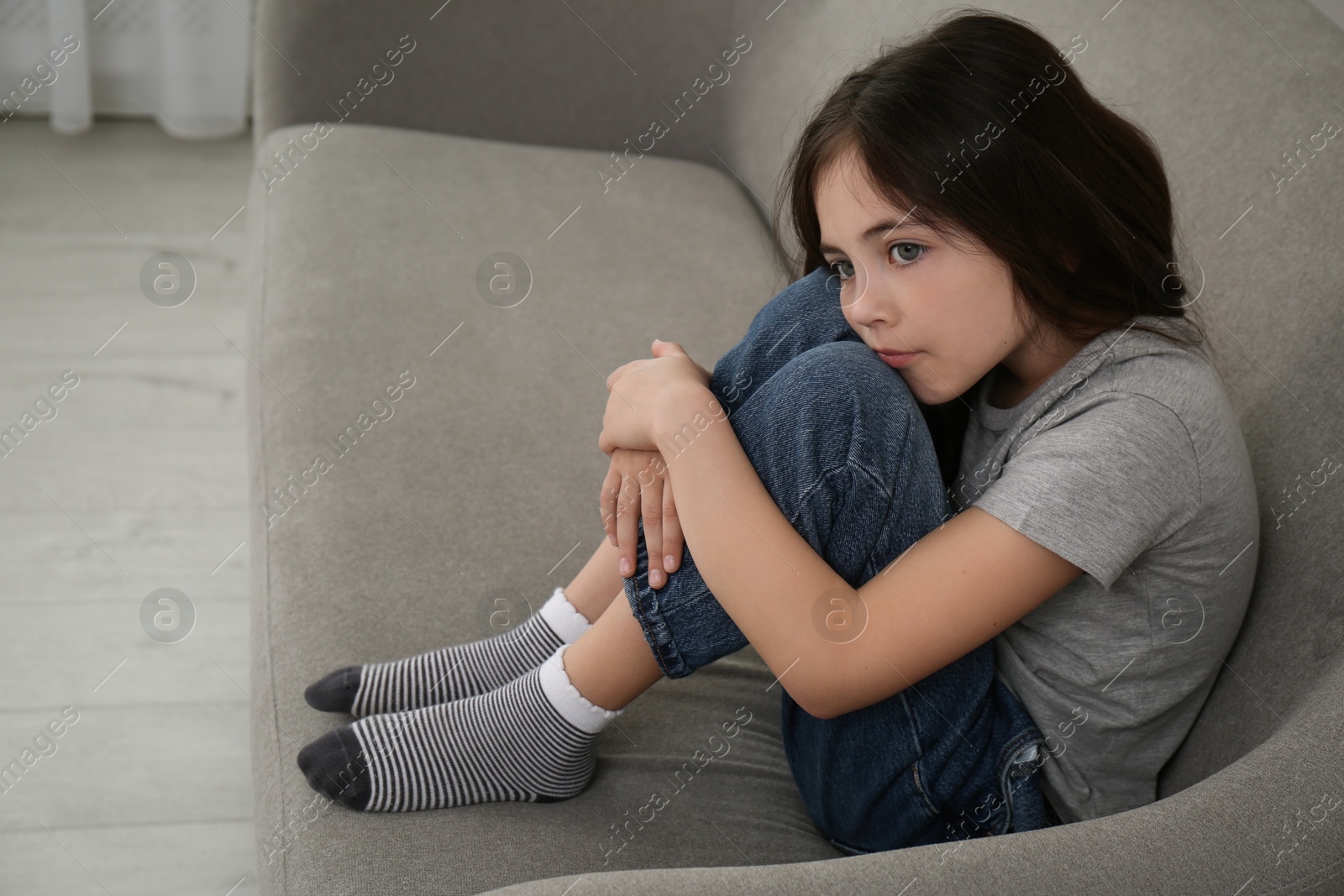 Photo of Sad little girl sitting on sofa indoors, space for text