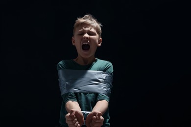 Photo of Scarred little boy tied up and taken hostage on dark background
