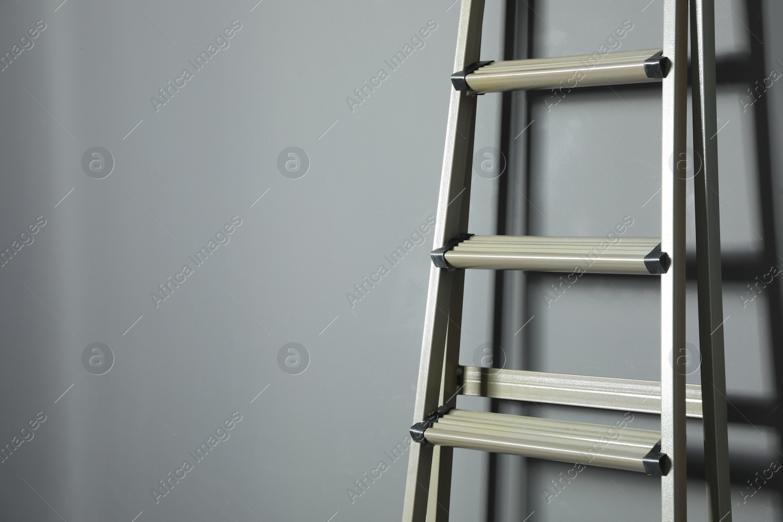 Photo of Metal stepladder on grey background, closeup. Space for text