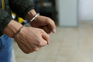 Photo of Man detained in handcuffs indoors, space for text. Criminal law