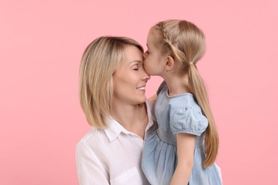 Photo of Daughter kissing her happy mother on pink background