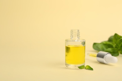 Photo of Glass bottle with basil oil, leaves and dropper on color background. Space for text