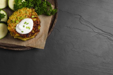 Photo of Delicious zucchini fritters with sour cream served on black table, top view. Space for text
