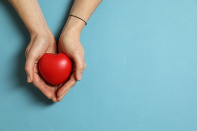 Photo of Woman holding red decorative heart on light blue background, top view. Space for text
