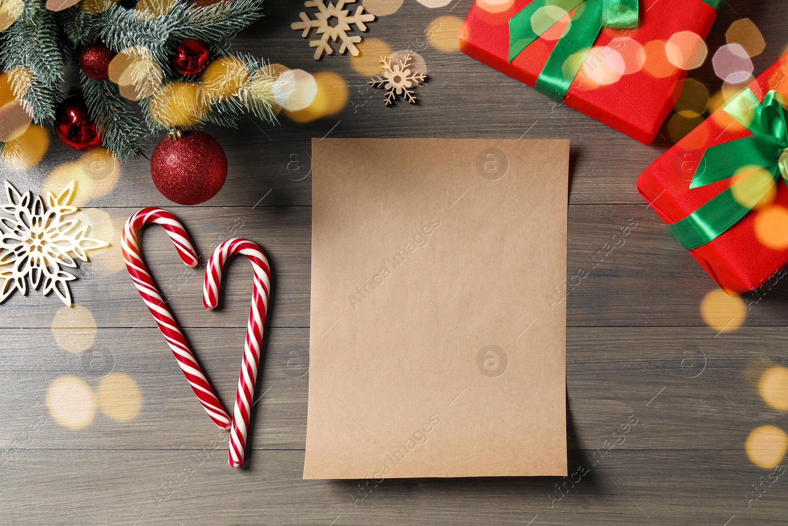 Photo of Flat lay composition with blank paper sheet, candy canes and Christmas decor on wooden table, space for text. Letter to Santa