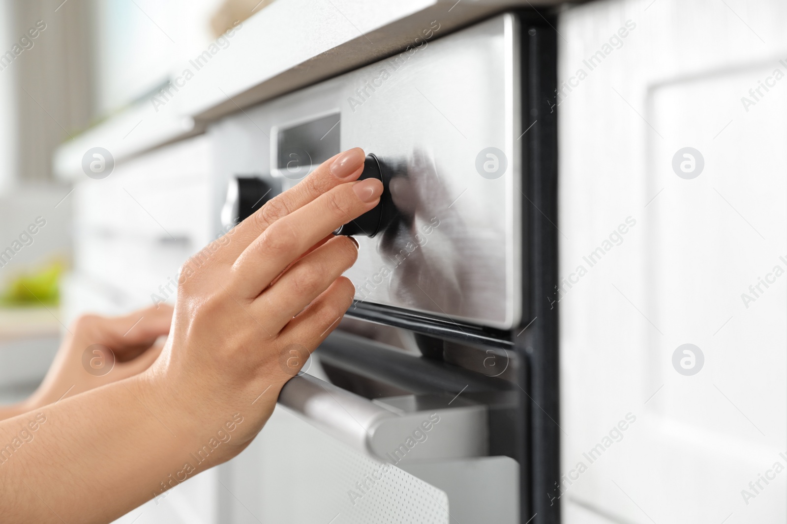 Photo of Woman regulating cooking mode on oven panel in kitchen, closeup