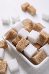 Different sugar cubes in bowl on white table, closeup