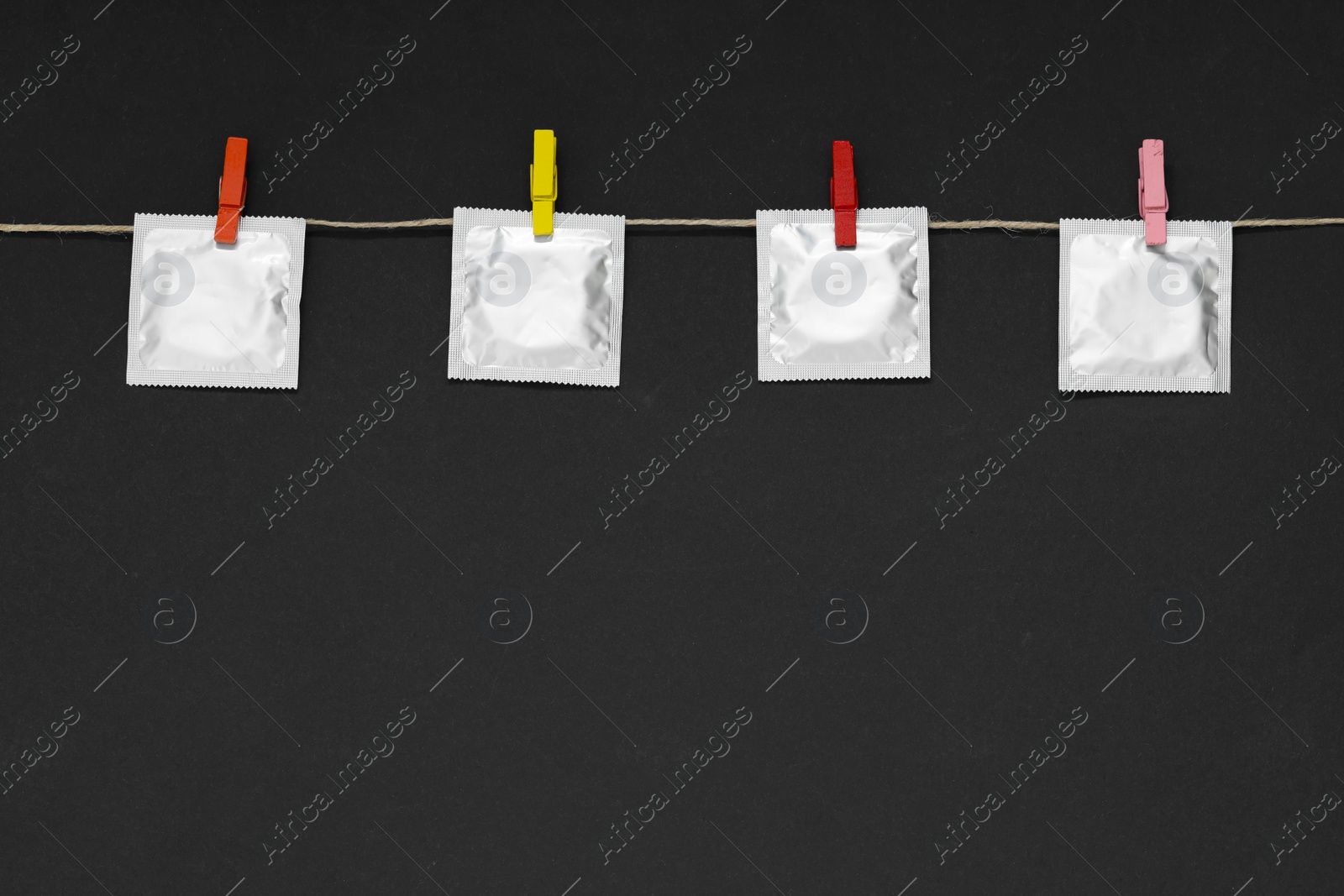 Photo of Clothesline with packaged condoms on black background, space for text. Safe sex