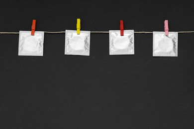 Clothesline with packaged condoms on black background, space for text. Safe sex