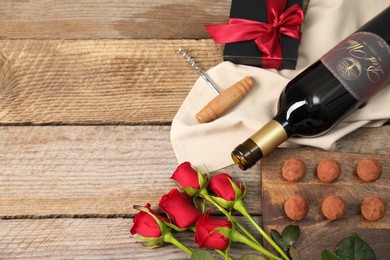 Photo of Bottlered wine, chocolate truffles, corkscrew, gift box and roses on wooden table, flat lay. Space for text