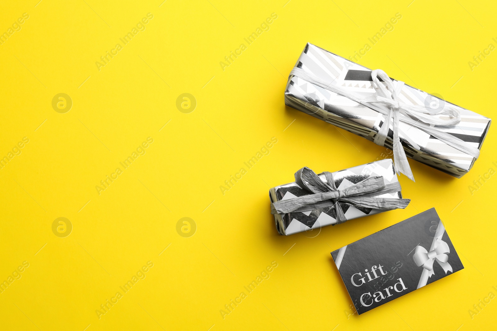 Photo of Gift card and presents on yellow background, flat lay. Space for text