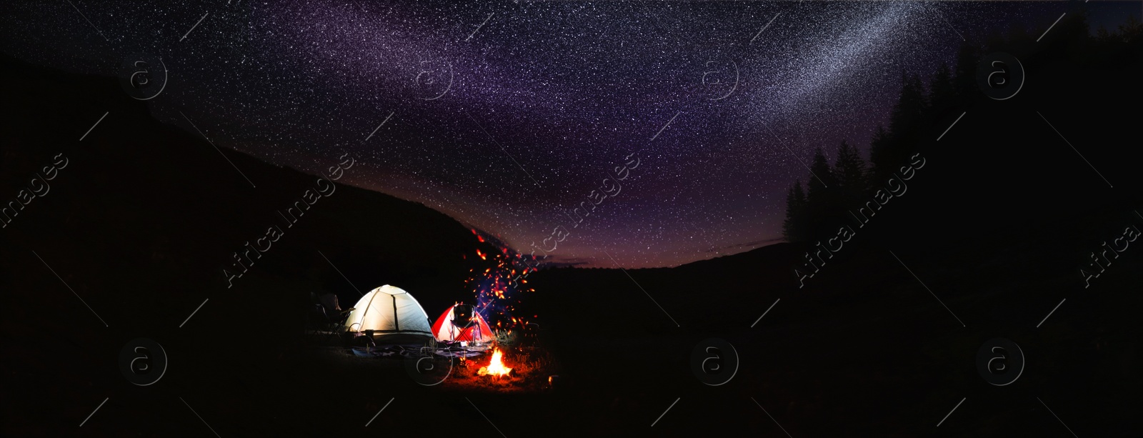 Image of Bonfire near camping tents outdoors at night. Banner design