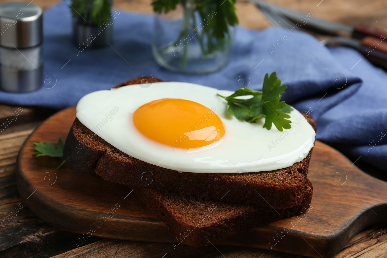 Photo of Tasty fried egg with parsley and rye bread on wooden board, closeup