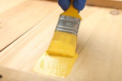 Photo of Worker applying yellow paint onto wooden surface, closeup