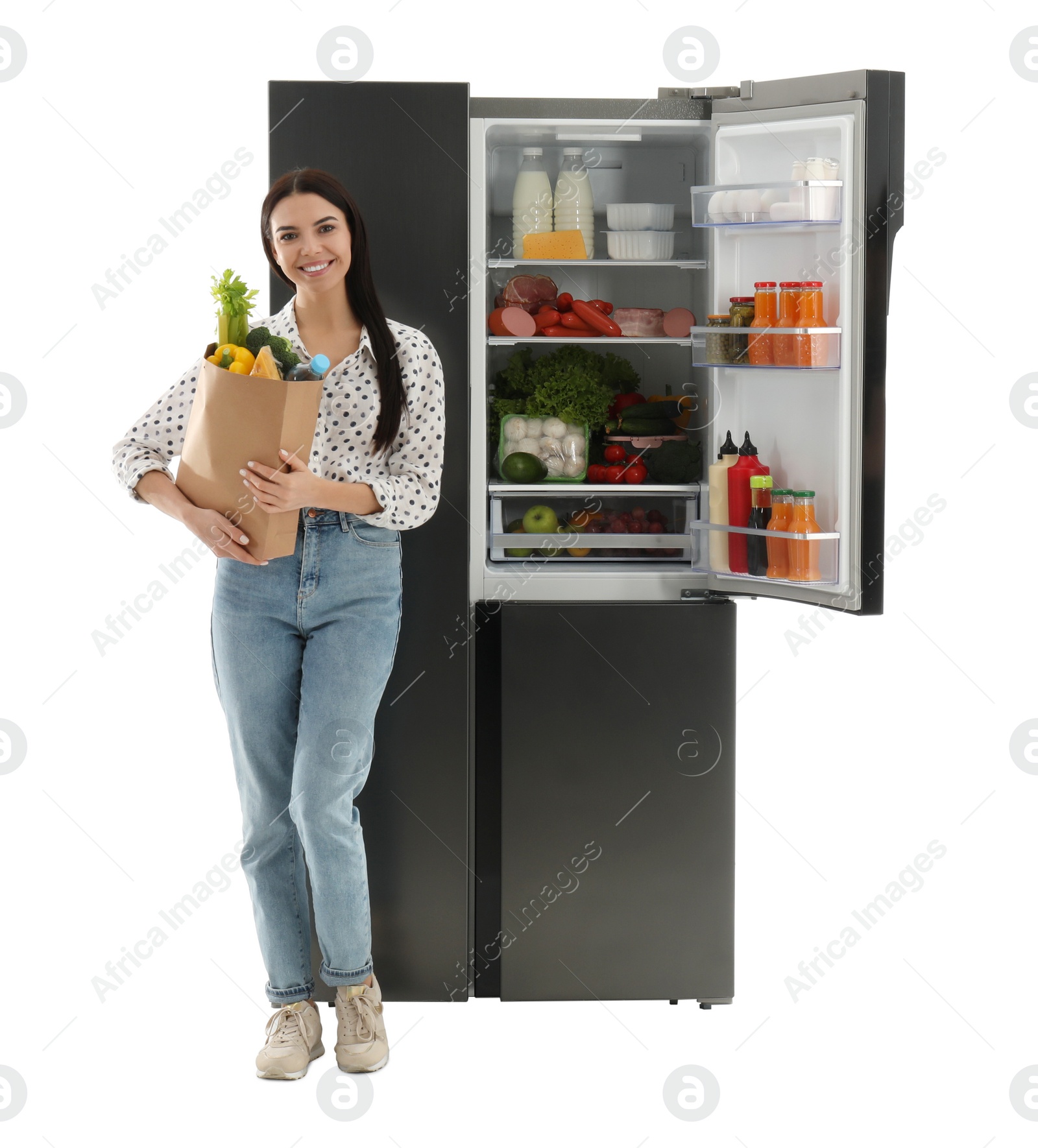 Photo of Young woman with bag of groceries near open refrigerator on white background